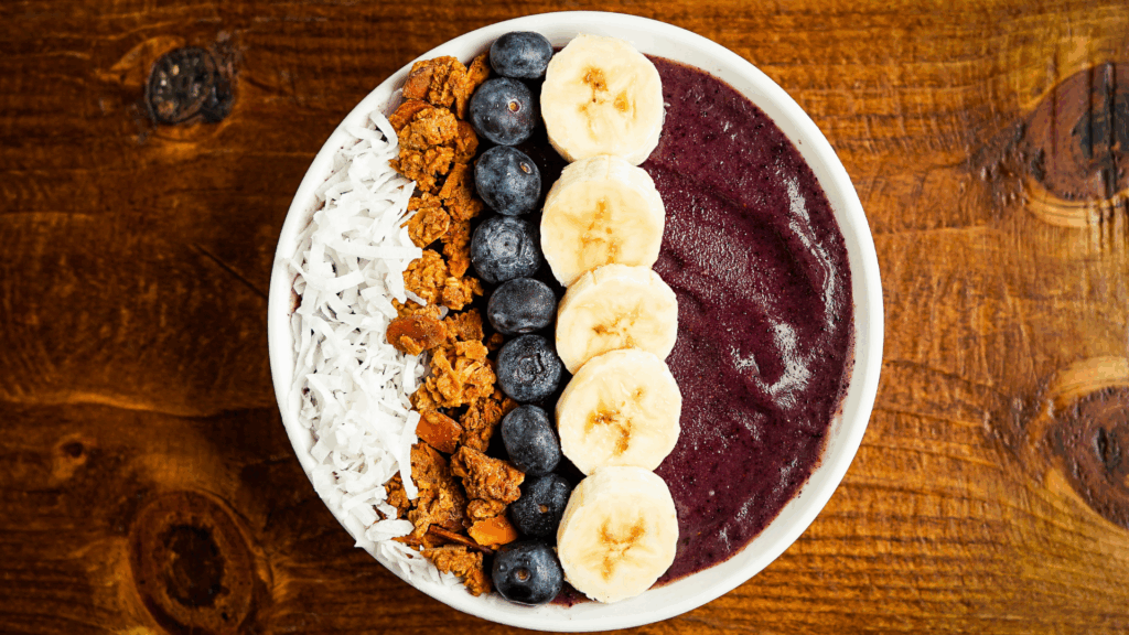Smoothie Bowl de Banana, Açaí e Proteína com Toppings Funcionais 1 Essa receita é ideal para quem precisa de energia rápida e limpa antes de treinar, trabalha muito ou busca um café da manhã vibrante e nutritivo. A base de banana e açaí fornece energia, antioxidantes e fibras. Já a proteína vegetal garante saciedade e suporte muscular. A textura é cremosa, os toppings trazem crocância e a sensação de estar comendo uma sobremesa saudável.
