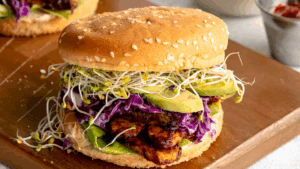 Uma explosão de sabores defumados e tropicais em um sanduíche nutritivo e funcional Este sanduíche combina a textura firme do tempeh com cogumelos e grãos integrais, tudo envolto em um molho barbecue caseiro. A salada crocante de repolho roxo e abacaxi traz frescor e equilíbrio, tornando esta refeição perfeita para um almoço leve ou um jantar descontraído.